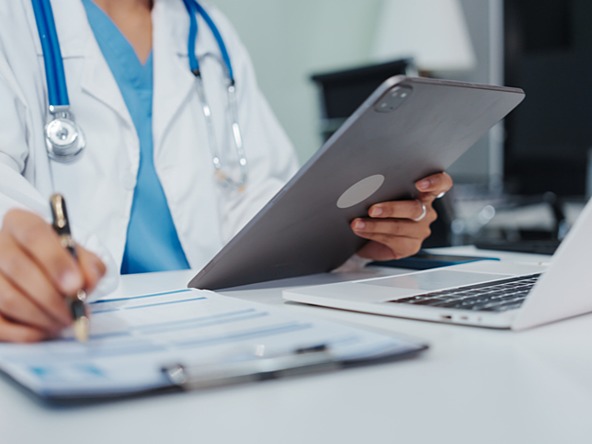 doctor reviewing notes on laptop, tablet and via a clipboard